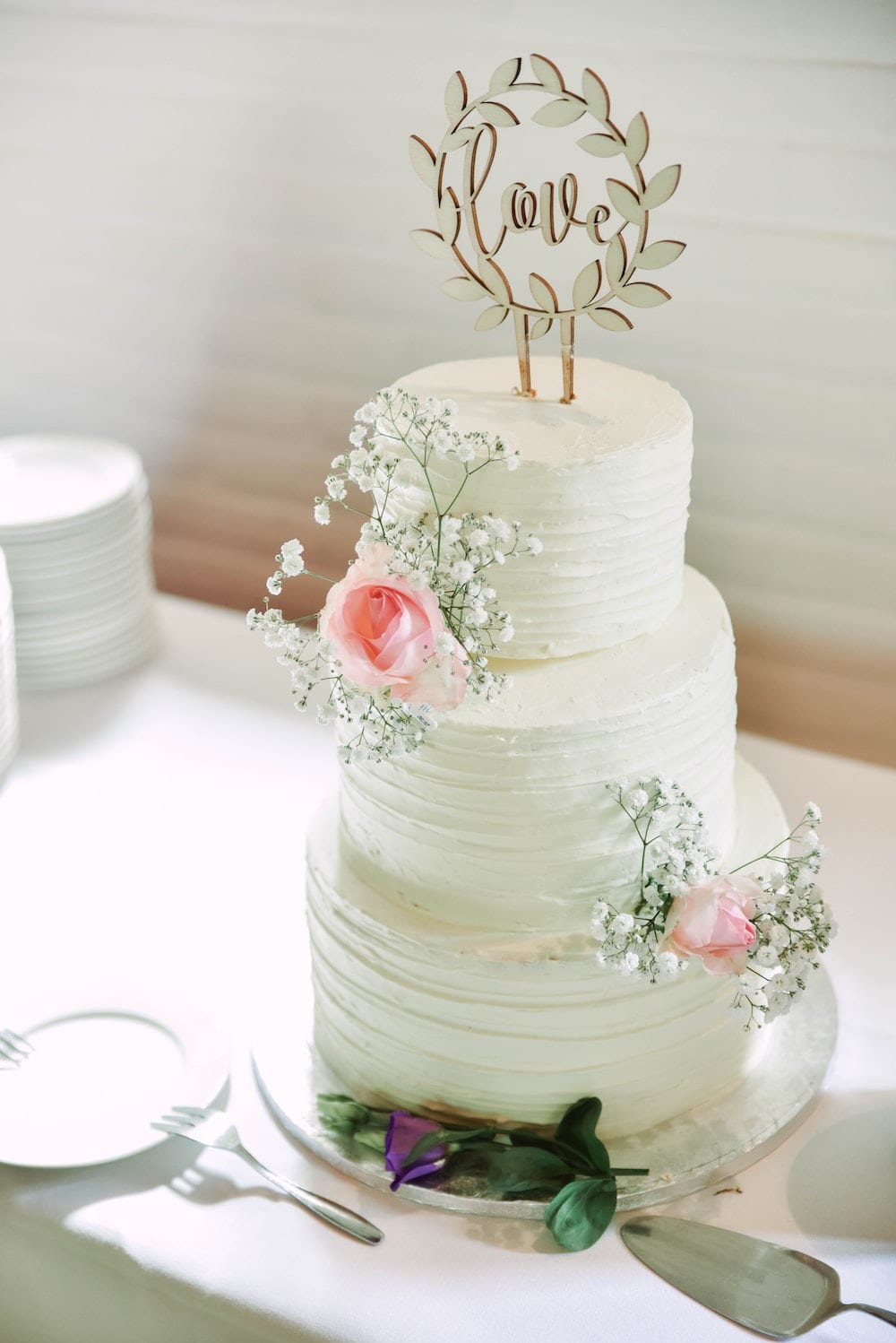 tiered white wedding cake with wooden love cake topper