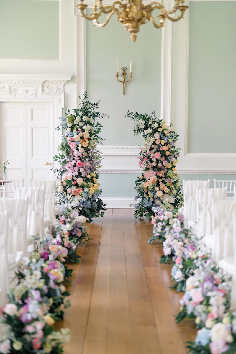 Pastel flower-lined aisle in the Green Room ready for a wedding ceremony at Botleys Mansion, Surrey